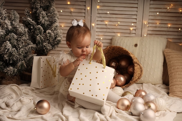 милая девочка в новогоднем костюме достает из подарочного пакета пудровые елочные шары
