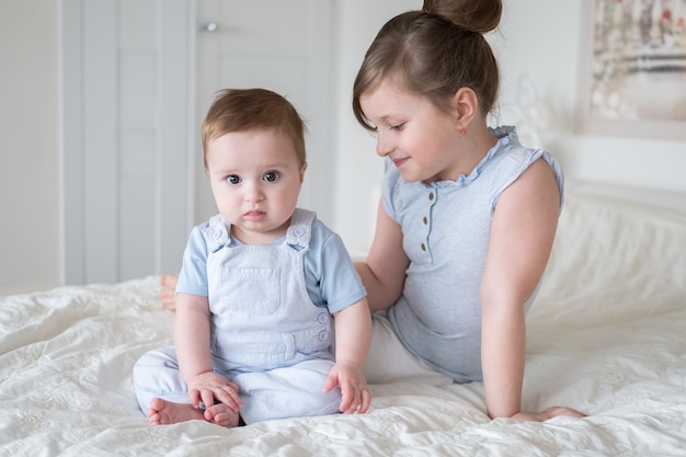 Cute little girl older sister with her baby boy brother at home sitting on bed