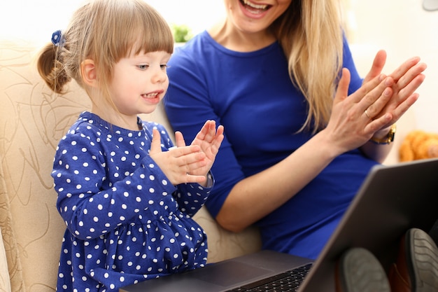 ママとソファの上のかわいい女の子は、ラップトップを使用します。