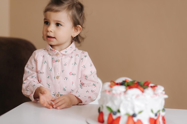 Cute little girl one and a hulf year old stand by delicious birthday cake Eighteen month old girl verry happy and laughs Vegetarian food Lactose free and gluten free