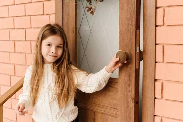 Cute little girl opens the door with a Christmas wreath