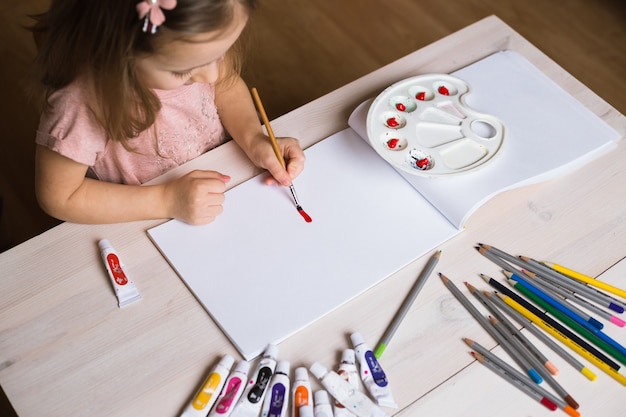 Photo cute little girl painting picture on home interior