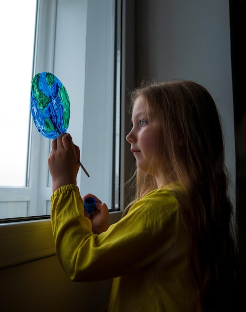 Foto carino bambina che dipinge il pianeta sulla finestra di casa happy earth day 22 aprile messaggio di saluto tempo libero familiare creativo