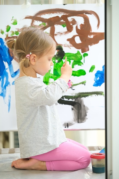 Photo cute little girl painting with various colors at home