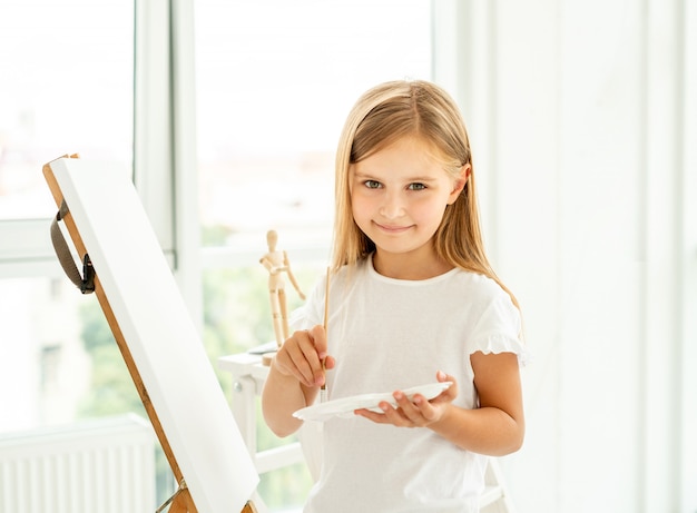 Милая маленькая девочка рисует на холсте