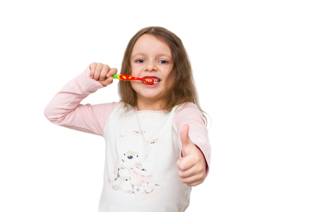 Cute little girl in pajamas brushing her teeth with a colored toothbrush