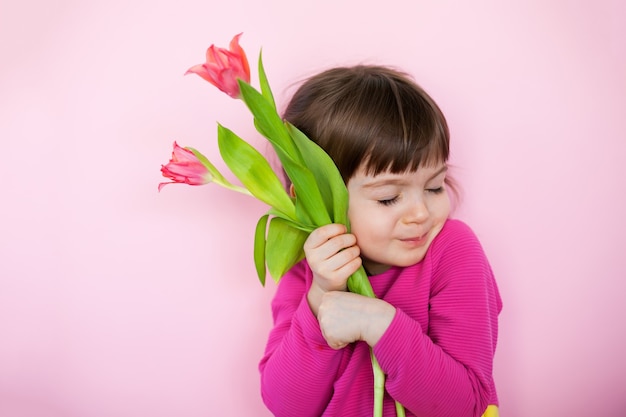 Bambina sveglia in vestito rosa che abbraccia i tulipani rosa