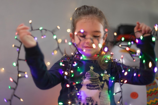 Cute little girl play with christmas lights with happy expression