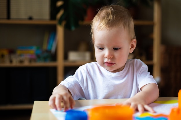 Cute little girl playing alone with many colorful plastic toys at home.