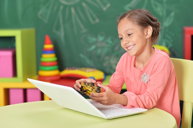 Bambina sveglia che gioca al gioco per computer sul computer portatile con il joystick