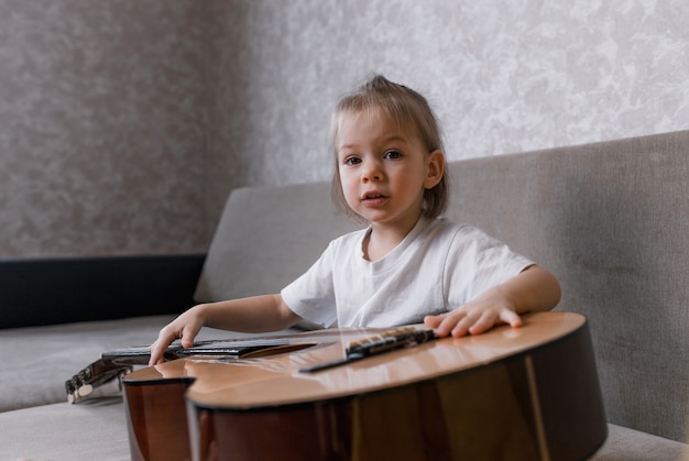 Bambina sveglia che gioca chitarra sul divano in camera. giochi e intrattenimento per bambini