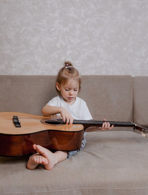 Cute little girl playing guitar on the couch in the room. children's games and entertainment