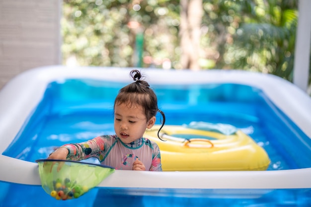 Cute little girl playing in an inflatable rubber swimming pool at home during quarantine period