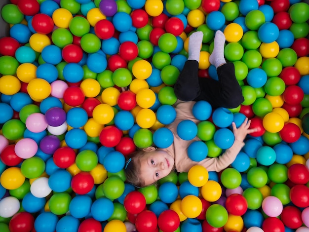 Cute little girl playing on multi coloured plastic balls in big dry paddling pool