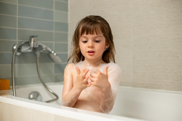 Милая маленькая девочка играет с пеной для ванны во время принятия ванны