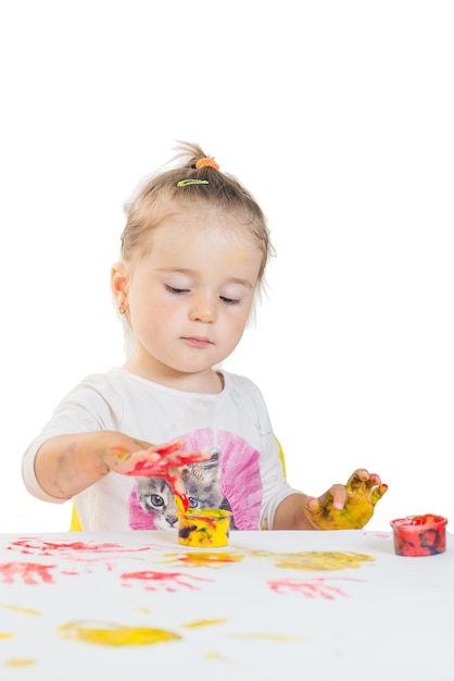 Cute little girl playing with colored paints on a white background