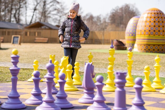 cute little girl playing with giant chess outdoors.