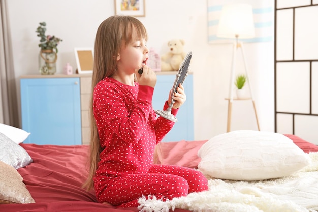 Cute little girl playing with her mother's cosmetic on bed