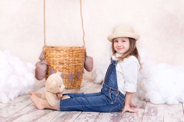 La bambina sveglia gioca in una stanza dei bambini con un orsacchiotto e un pallone.