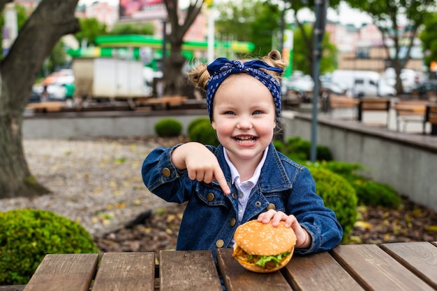 Cute little girl pointed on burger before eat in cafe outdoors