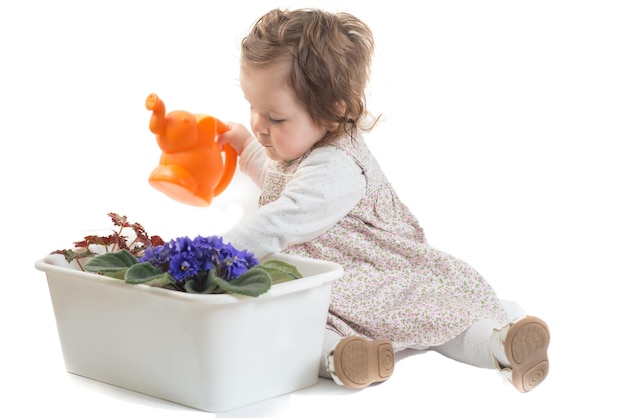 Милая маленькая девочка наливает цветы в горшок на белом фоне
