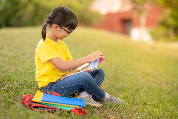 Cute Little Girl Reading Book Outside on Grass