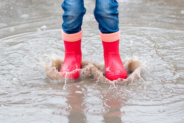 A cute little girl red boots jump in puddles and has a fun\
happy childhood early spring emotions