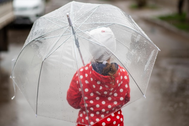 A cute little girl in a red cape red boots and a white hat jump in puddles and has a fun