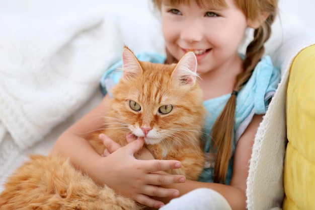 Cute little girl and red cat on sofa closeup