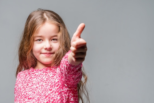 Cute little girl in a red dress shows thumb up on a yellow background toned