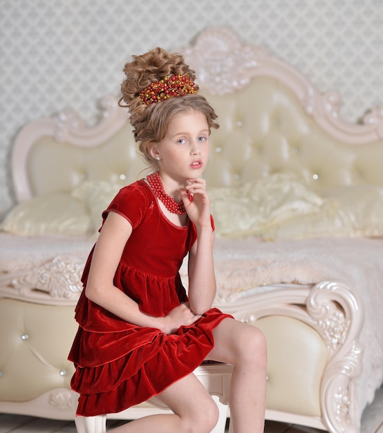 Cute little girl in red dress sitting in bedroom