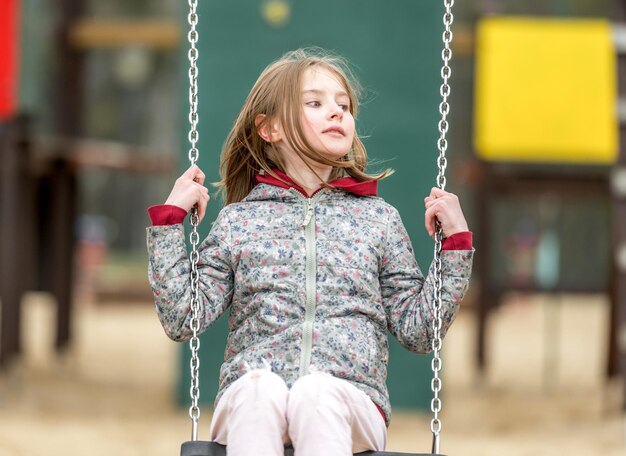 Cute little girl riding a chain swing in a autumn park
