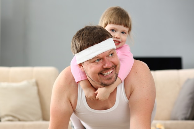 Cute little girl riding her father at home playing