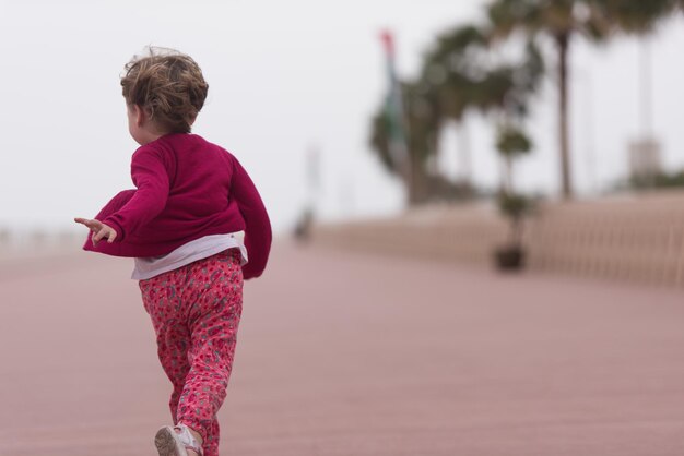 Cute little girl running and cheerfully spend her time on the promenade by the sea