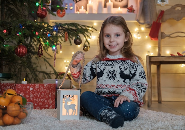 Bambina sveglia in un maglione scandinavo all'albero di natale. il concetto di una festa in famiglia del natale e del nuovo anno