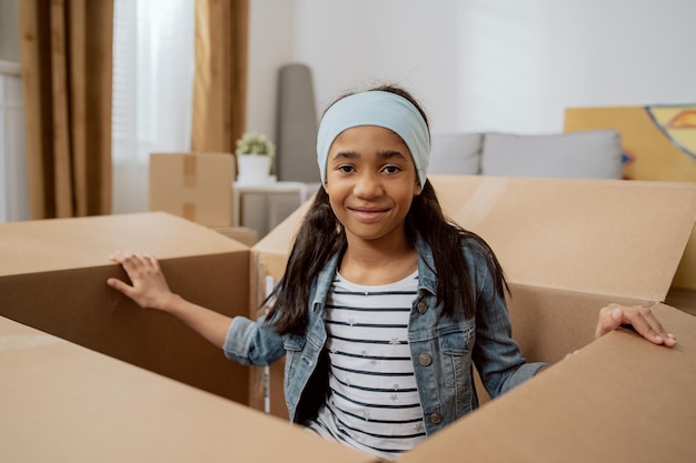 A cute little girl sits in a cardboard box used for packing things during a move