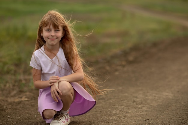 Cute little girl sits on the countryside empty road