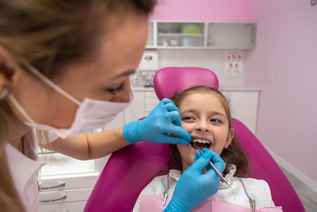 Cute little girl sits on a dental chair and treats aching teeth makes a face