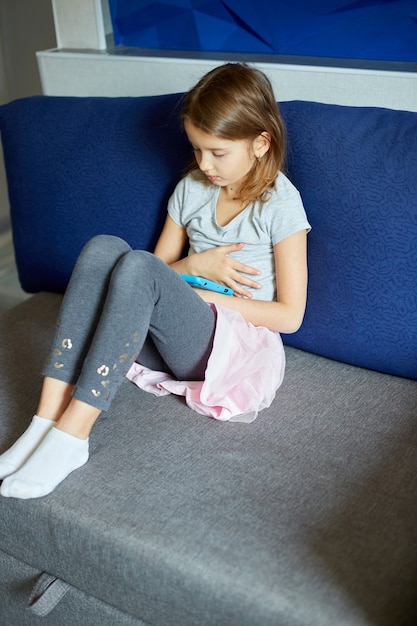 Cute little girl sitting on couch, Kid addicted to technology, enjoying playing online game on digital tablet computer, using applications, web surfing information at home,