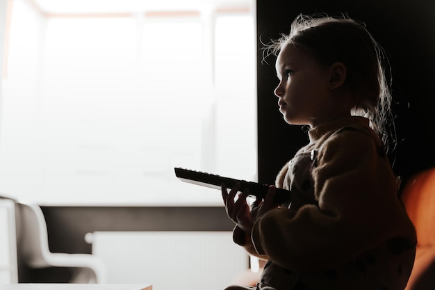 Cute little girl sitting on the couch while watching tv at home
in the evening beautiful young child daughter girl watch television
on living room concept video game entertainment family relax