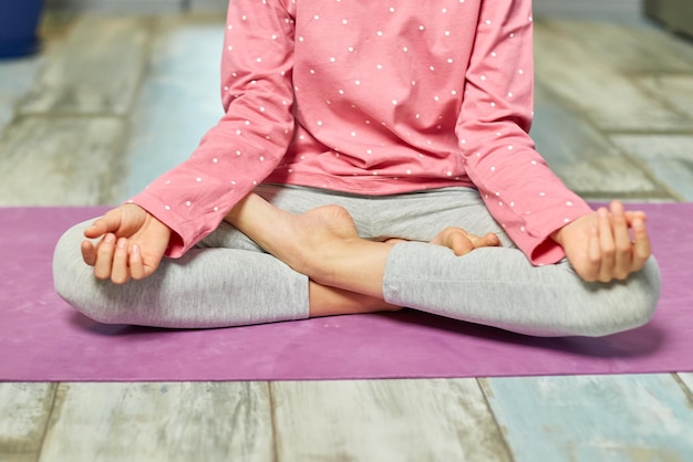 Photo cute little girl sitting on fitness mat in a lotus position while doing yoga at hom