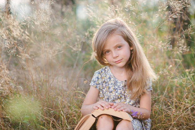 Photo cute little girl sitting on the grass and reading a book in the