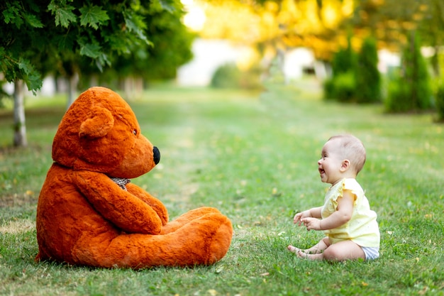 Cute little girl sitting on the grass with a big teddy bear