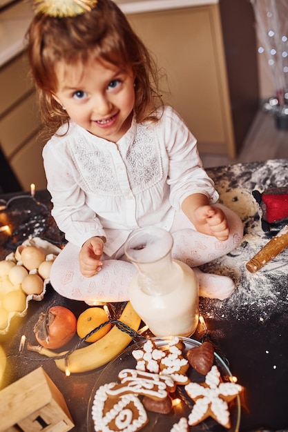 Cute little girl sitting and have fun on the kitchen with food.