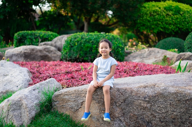 Cute little girl sitting on large rock in the park