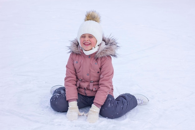 Фото Милая маленькая девочка сидит на льду с коньками после падения и смеется