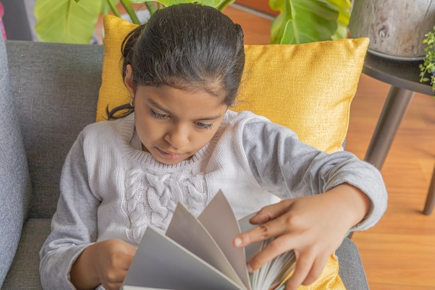 Cute little girl sitting on a sofa and reading a book