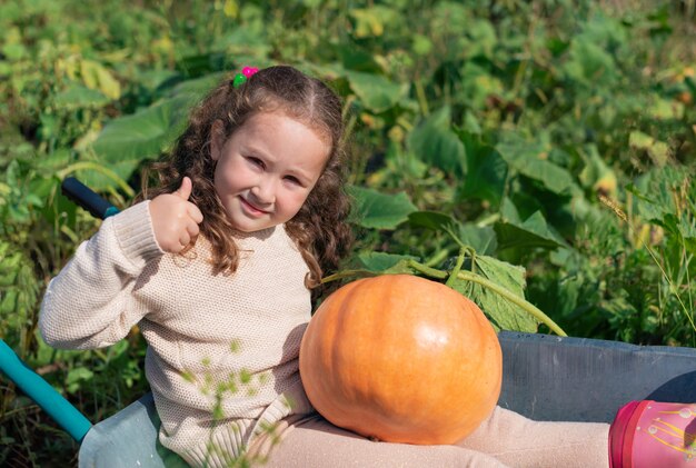 Cute little girl sitting with a pumpkin in a garden cart