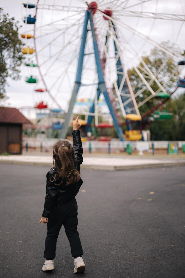 公園の女の子の観覧車の前に立っているかわいい女の子は、彼女がしたいことを示しています