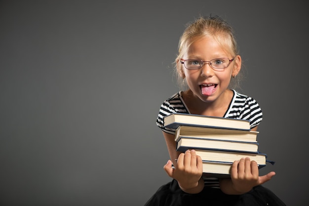 Cute little girl standing and holding books. Studio shutting. Grey background. Looking at camera.